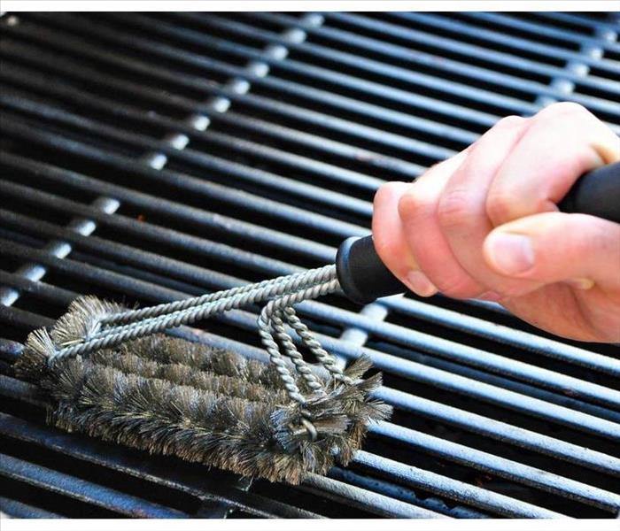 Hand holding a wire brush and cleaning the inside of a grill